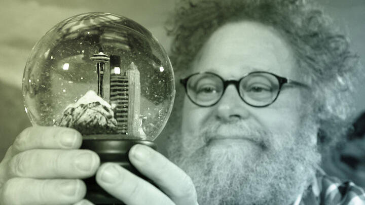 Knute Berger (of Mossback&#039;s Northwest) holds and gazes into a snowglobe containing Seattle city skyline